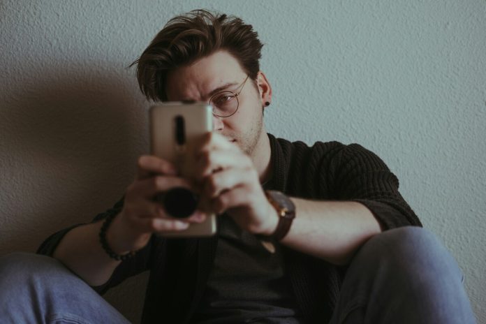 Jaunietis, telefons, brilles, sociālie tīkli